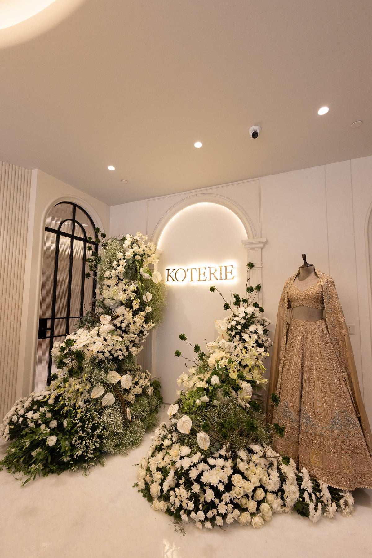 Inside the Koterie store: the lit Koterie sign in an arch, white flowers and a gold bridal lehenga